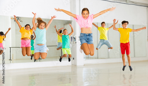 Group of happy sporty kids training in modern dance studio, jumping together.