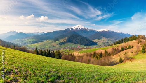 panorama of mountainous rural landscape with village in the valley carpathian countryside scenery with arable on hills in front of borzhava ridge with snow capped top on a sunny morning in spring