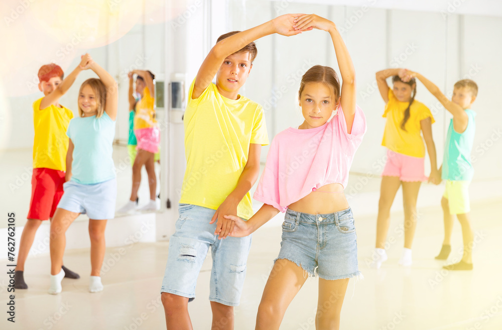 Fototapeta premium Portrait of positive tweenagers practicing slow ballroom dances in pairs in choreographic studio.