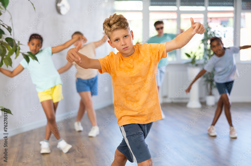 Man child dances waacking in choreographic school, group of young people in sportswear trains together with their classmates in gym before competitions, battle