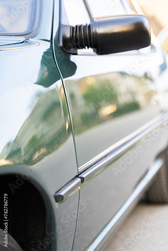 A close up shot of a green retro car door featuring a sleek black side mirror. The vehicle also showcases its automotive parking light, tire, hood, and lighting system