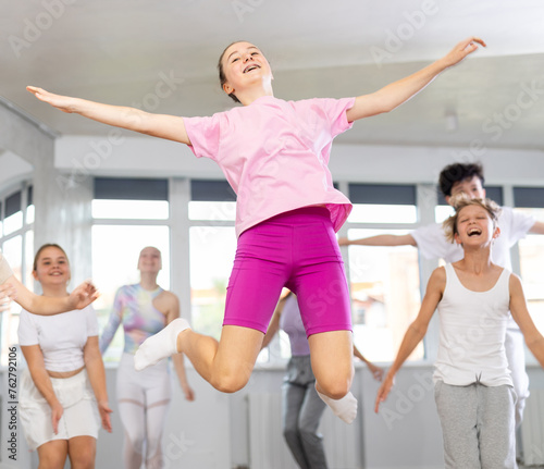 Female teenager engaged jumping into air in fitness studio with friends, group of youthful friends bob up and down during dance class. Teen people in good mood actively move and dance at choreography.