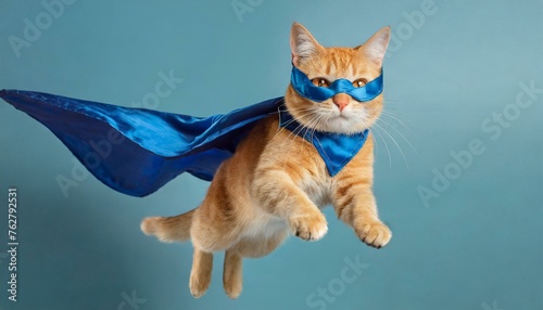 Feline Hero: Cute Orange Tabby Kitty Soaring in Blue Cloak and Mask on Light Blue Background © Ashfaq