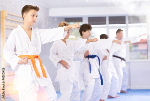 Willing junior boy wearing kimono training karate techniques in group during workout session