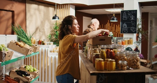 Woman in zero waste shop buying fruits, checking products before making purchase, ensuring they are pesticides free. Vegan client verifying apples in local bio food store are organic, smelling them