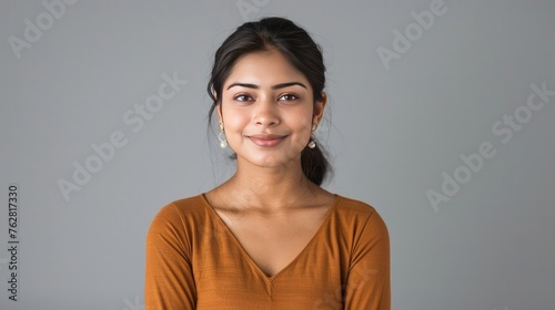 Smiling attractive young adult indian woman in casual wear standing isolated on grey studio background with copy space. Student professional hindu lady model looking at camera with happy face