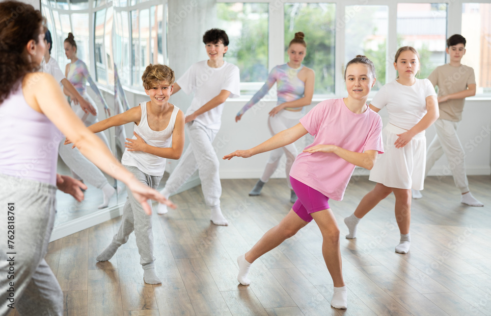 Obraz premium Girl teen performs modern dances repeats movements of unrecognizable teacher together with friends during lesson at choreographic school. Hobbies, active pastime