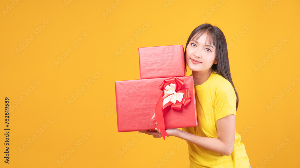 Cheerful asian woman holding two red gift box for celebration standing copy space over isolated yellow background. Positive joyful young girl showing shopping gift for Christmas or happy new year. Cheerful asian woman holding two red gift box for celebration standing copy space over isolated yellow background. Positive joyful young girl showing shopping gift for Christmas or happy new year.