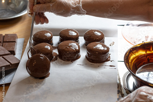 Organizando doces que acabaram de ser cobertos por chocolate com uso de luvas e utensílios de cozinha photo