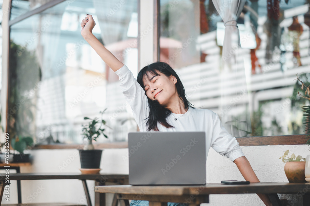 A woman stretches with a contented smile during a break from work, surrounded by the soothing ambience of her bright, plant-adorned home office. A woman stretches with a contented smile during a break from work, surrounded by the soothing ambience of her bright, plant-adorned home office.