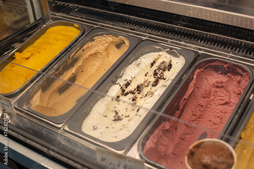 Multiple metal trays containing dairy mango, cherry, raspberry, mocha, vanilla, chocolate and caramel creamy gelato ice cream for sale in an ice-cream parlor. The various flavors are for round scoops.