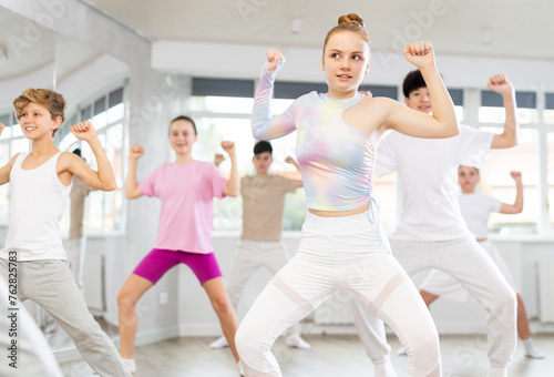 Female teen performs choreographic exercises and teaches energetic mobile social house dance together with friends. Young girls and guys in repeat movements, train in spacious studio