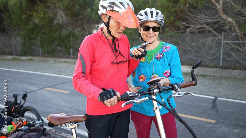 Senior and mature woman take a break while biking to look at a map on their phone for directions. Making a call.