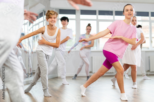 Girl teen performs modern dances repeats movements of unrecognizable teacher together with friends during lesson at choreographic school. Hobbies, active pastime