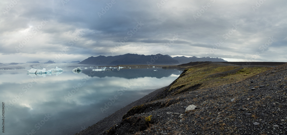 The shore at the edge of Jokulsarlon glacier lagoon leading towards the mountains and Vatnajokull National Park in the background 