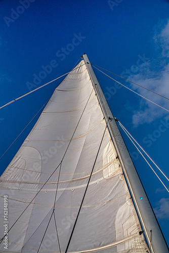 Close-up of a sailboat mast soaring into a clear blue sky, highlighting details of the sail and rigging