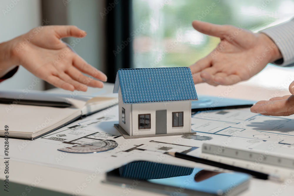 Fototapeta premium An engineer is working with a colleague in an office is discussing a model of a house designed as a prototype for a client and is reaching agreement that the design is what the client wants.