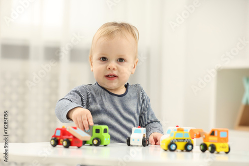 Children toys. Cute little boy playing with toy cars at white table in room