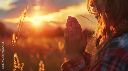 A girl's hands clasped in prayer and praise as the sun sets. Christianity as a religion. 