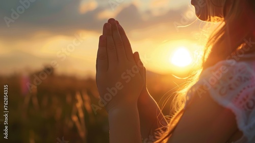 A girl's hands clasped in prayer and praise as the sun sets. Christianity as a religion. 