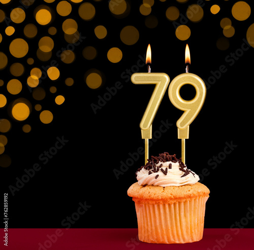 Birthday candle with cupcake - Number 79 on black background with out of focus lights photo