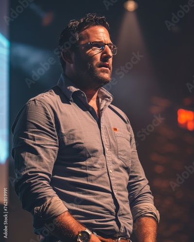 A man in a blue shirt and glasses stands in front of a projection screen © jiawei