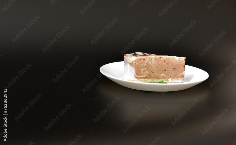 White ceramic plate with a slice of cream cheesecake with mint leaves on a black background.