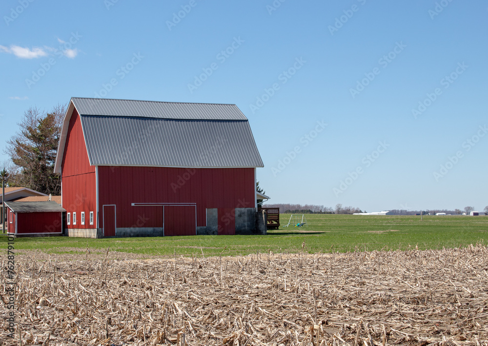 Obraz premium A large red barn next to a cornfield after harvest.