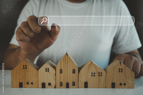 Hand touching search bar for information data about home on top of a model wood house. Search advertising for rent or buy a home. Search engine optimization. Planning to buy property.