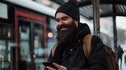 Happy bearded man using smartphone at bus station for modern technology concept