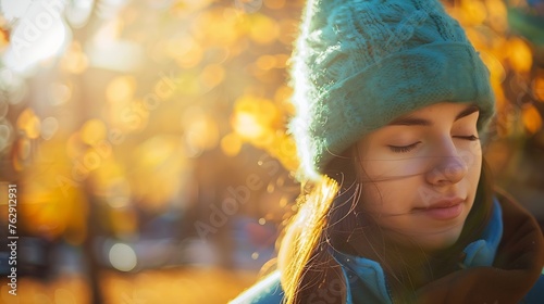 Calm girl in blue coat and green hat and coat closing eyes while spending sunny day on blurred background of autumn park in a cold day in donostia san sebastian spain : Generative AI photo