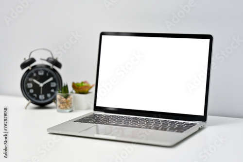 Close up view of simple workspace with laptop and clock on white table.