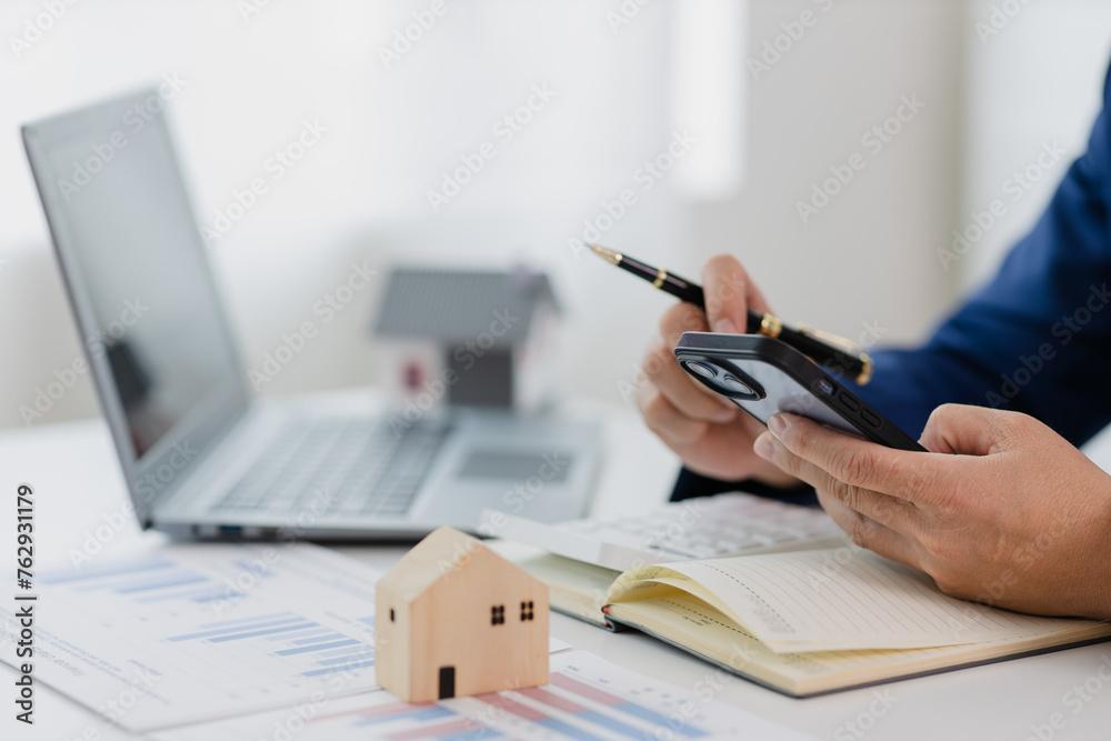 Fototapeta premium Man in a suit doing property tax calculations using a calculator of a house model