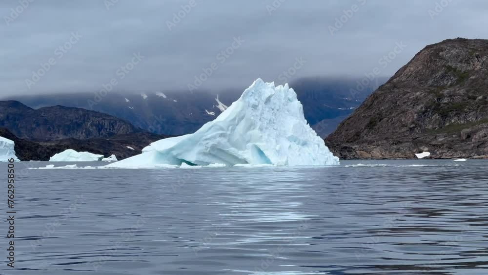 Iceberg is changing position after breaking off. Bear Islands, Scoresbysund, Greenland. Iceberg is changing position after breaking off. Bear Islands, Scoresbysund, Greenland.