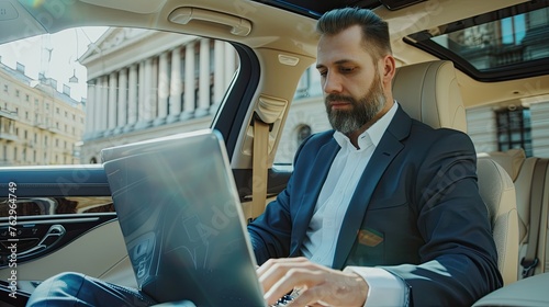 Businessman working on laptop computer while sitting in luxury car. © morepiixel