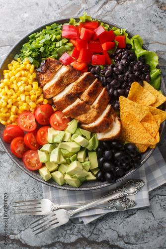 Southwest Salad or Santa Fe Salad is the perfect blend of fresh ingredients like lettuce, tomatoes, corn, black beans and juicy chicken breast closeup on the plate on the table. Vertical top view from