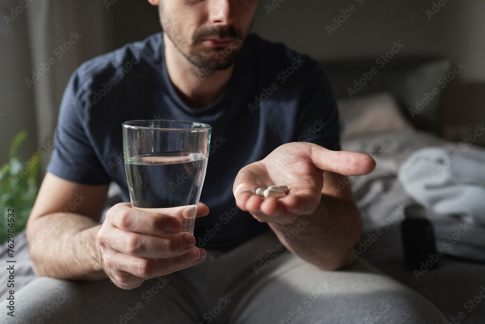 Man sitting on bed and about to take pills