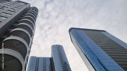 Modern tall building with unique design. Low angle view of abstract curve lines and sky. Geometric facade with glass and steel. City skyscrapers bottom view against gray sky. Concept of exterior.