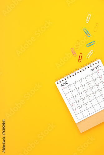 April 2024 desk calendar and paper clips on yellow color background.
