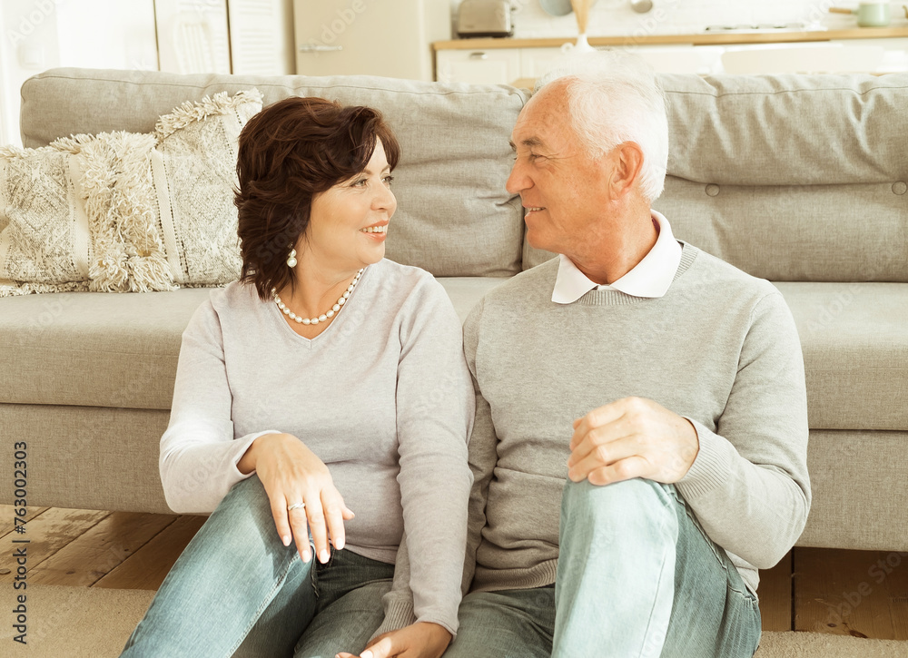 Obraz premium An elderly couple hugging while sitting on the floor of the living room. Relationship and family concept.