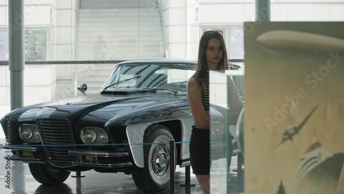Slowmotion - Attractive young girl walks across gallery in front of vintage car photo