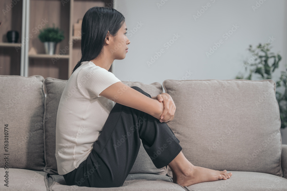 Young Asian woman sitting on sofa, depression, distressed, touches face and head, eyes closed. tired, sick, and stressed, possibly grappling with bad news or crisis, experiencing headache or migraine Young Asian woman sitting on sofa, depression, distressed, touches face and head, eyes closed. tired, sick, and stressed, possibly grappling with bad news or crisis, experiencing headache or migraine