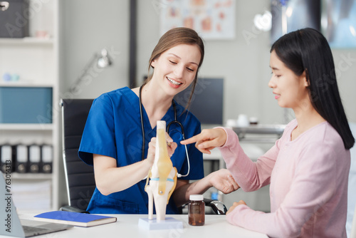 Caucasian female doctor explain to asian female patient using knee bone model at desk in medical room, medical learn aid anatomy instrume, Knee Osteoarthritis, loose patella