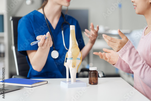 Caucasian female doctor explain to asian female patient using knee bone model at desk in medical room, medical learn aid anatomy instrume, Knee Osteoarthritis, loose patella photo