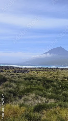 Amazing view of the coastline of Lajes Do Pico. The red windmill is an icon of Portugal. Amidst large waves, you can see the volcano or Mount Pico. Vertical video  photo