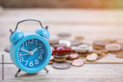 Coins and blue alram clock on wood table background.