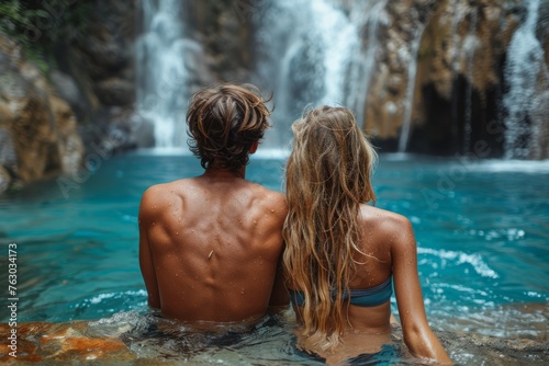 A couple enjoying a serene moment together in a natural hot spring with a waterfall in the background. © Good AI
