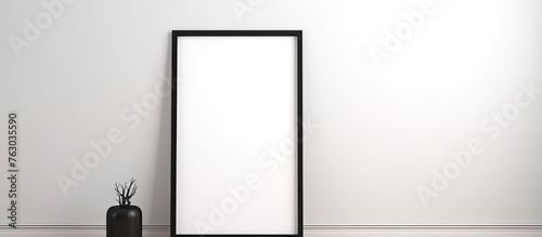 A rectangular fulllength mirror made of wood and glass leans against a white wall next to a vase, creating an artistic display. The monochrome photography captures the tints and shades of the scene photo
