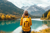 young female hiker with a yellow backpack gazing at a scenic mountain lake