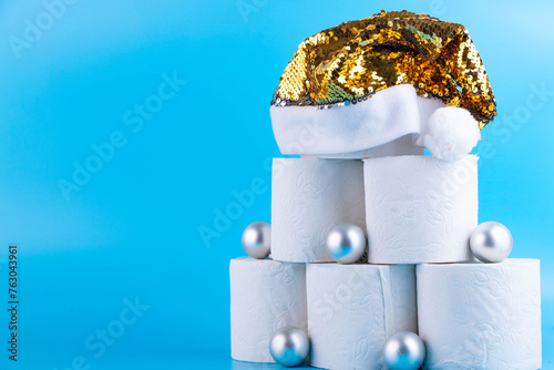 Christmas tree made of toilet paper rolls decorated with shiny balls and a golden santa claus hat on a blue background photo